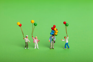 Miniature people : Happy family holding balloon on green background
