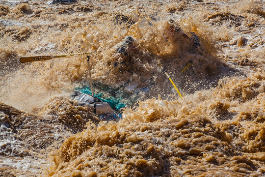 Boatman gets smothered by a giant wave of water as he rows his raft through the notoriously huge V wave in Lava Falls Rapid on the Colorado River. Grand Canyon National Park.
