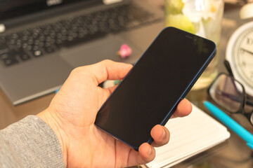Man uses smartphone on home interior background with laptop, blank screen mockup concept photo