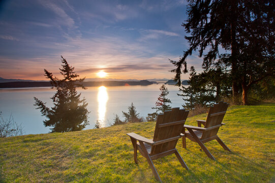 Two empty Adirondack chairs at sunrise overlooking Puget Sound and the Cascade Mountains. Whidbey Island, WA.