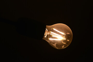 Stara i brudna  żarówka elektryczna słabo świeci żółtym światłem. 