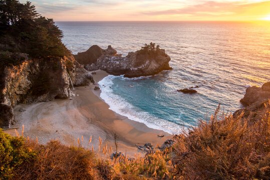 The sun sets in a spectacular fashion as the McWay Falls drop eighty feet down to the sand along California's dramatic Big Sur coast.