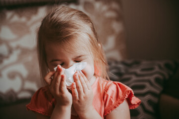 Toddler girl blowing her nose with a tissue