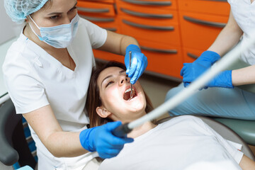 Medical treatment at the dentist office. Female dentist and assistant in dental office examining young woman with tools in dental clinic