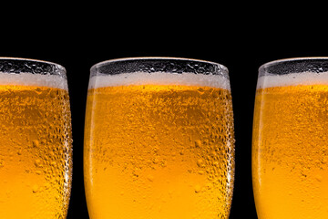 A row of beer glasses with beer on a black background. Space for text and logo. Drops of water trickle down the glass.