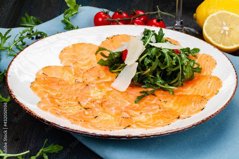 Wall mural Salmon carpaccio served with arugula leaves, parmesan cheese and cherry tomatoes on white plate.