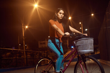 Obraz na płótnie Canvas hermosa Mujer joven maneja feliz en bicicleta por un parque por la ciudad. Modelo ciclista en mascarilla 