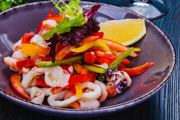 Salad with squid, bell pepper and onion on gray plate