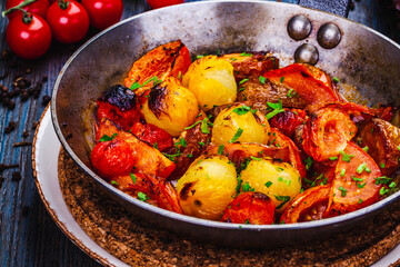 Roasted cherry tomatoes in cast iron skillet on wooden table.