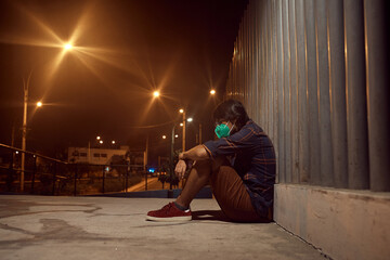Hombre triste sentado en el suelo afuera de un hospital. Persona enferma durante pandemia mundial. Hombre solo en la noche con mascarilla.