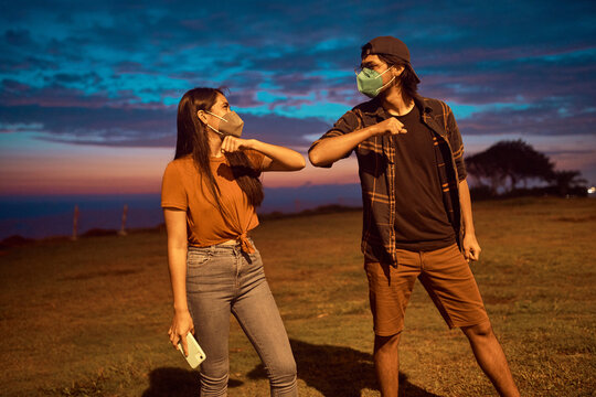 dos jovenes realizan el protocolo de saludo con codos para evitar contagios. Jovenes en el parque con mascarillas