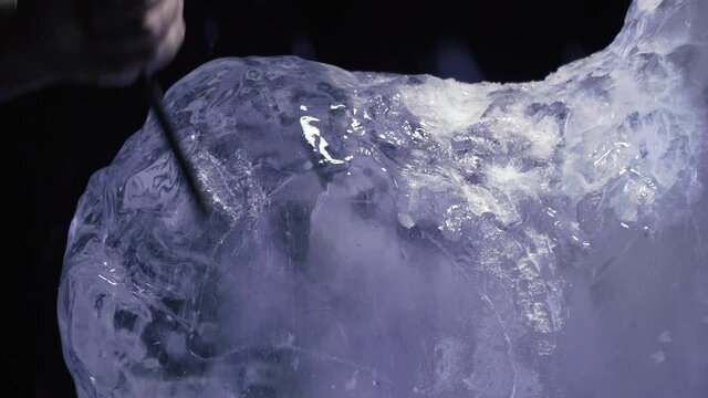 Artist is breaking off pieces of ice to shape up an ice sculpture with a chisel