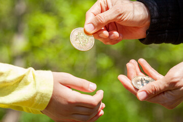 A child is asking for pocket money and her parent is giving a bitcoin coin in response.  Concept image in family setting for using cryptocurrency in day to day transactions instead of regular cash.