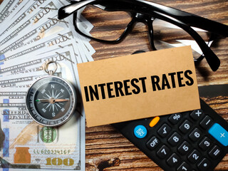 Business concept.Text INTEREST RATES with compass,glasses,banknote and blur calculator on a brown wooden background.