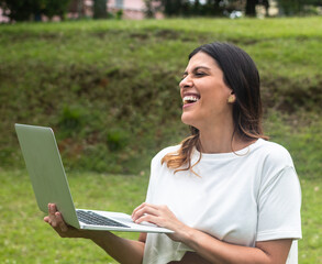 latina woman standing with laptop in park