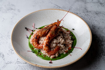 Colorful and appetizing photo of modern italian risotto with basil sauce and two king prawns in a shell, close, top photo