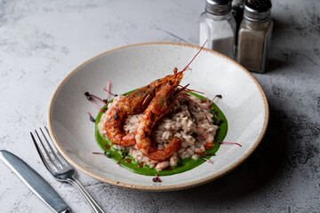 Colorful and appetizing photo of modern italian risotto with basil sauce and two king prawns in a shell, close, top photo