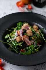 Bacon and rocket salad with croutons on a black wide plate