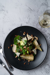 Fusion cuisine salad with pear and blue cheese with a glass of wine on a grey stone table, above shot with copy space