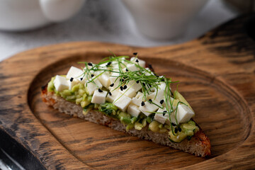 A single avocado toast with feta cheese and sprouts on a wooden board, close up, ad, advertisement,...