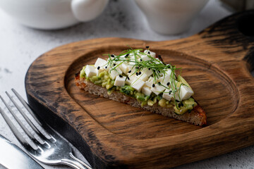 A single avocado toast with feta cheese and sprouts on a wooden board, close up, ad, advertisement,...