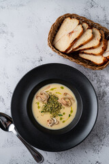 Above shot of a cream cheese soup with fettuccine nests in a black bowl, grey stone background, menu photography
