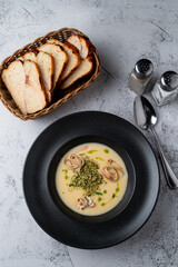 Fatty cheese soup with cheddar and cream, menu photography setting with salt and pepper and bread basket aside