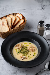 Fatty cheese soup with cheddar and cream, menu photography setting with salt and pepper and bread basket aside