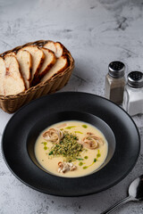 Fatty cheese soup with cheddar and cream, menu photography setting with salt and pepper and bread basket aside