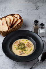 Fatty cheese soup with cheddar and cream, menu photography setting with salt and pepper and bread basket aside