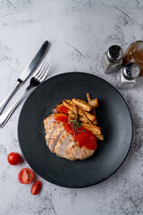 Above menu photography shot: poultry breast grilled with potato slices on a light grey stone table