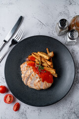 Above menu photography shot: poultry breast grilled with potato slices on a light grey stone table