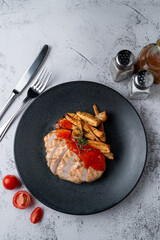 Above menu photography shot: poultry breast grilled with potato slices on a light grey stone table