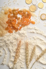 Flour, wheat, rice, raisins and coins on a white background