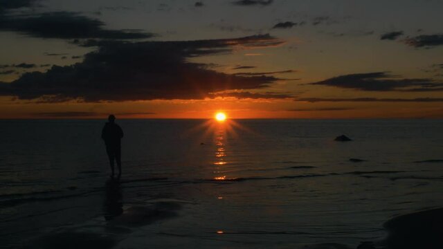 Silhouette man standing in shallow sea enjoying a summer sunset, in Scandinavia