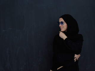 Young muslim in traditional clothes or abaya and sunglasses posing in front of black chalkboard