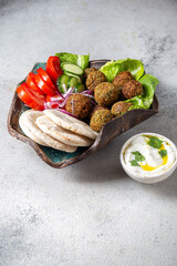 Falafel, fresh vegetables and pita bread on clay plate, gray background