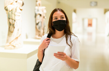 Attentive visitor girl in a protective mask, who is in the museum during the pandemic with an...