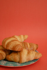 Front shot of delicious homemade golden croissants in turquoise blue plate on coral background