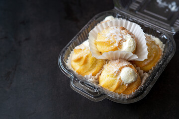 Cream puffs filled with pastry cream and sprinkled with powdered sugar in a transparent clear container.