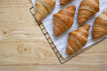 Flatlay of delicious homemade golden croissants on white baking paper and pine wood table