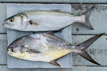Two fishes caught in the ocean on a plate on the wooden stairs. Pompano fish and bluefish....