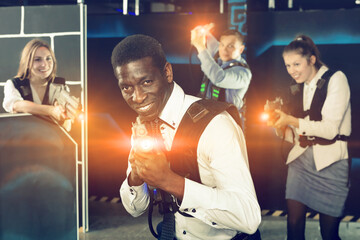 African American man in business suit holding the his laser gun and playing laser tag with his associates