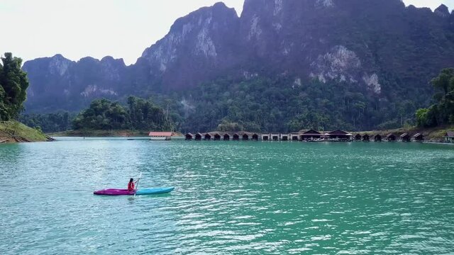 Cute Asian Girl Chilling Kayaking in front of Floating Houses in Cheow Lan Lake, Thailand. Drone.