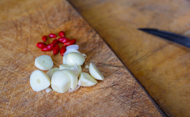 Close up and selective focus shot of peeled garlic and red paprika on cutting board with blurred background of knife shows traditional cuisine for home cooking of asian people, especially Thai food.