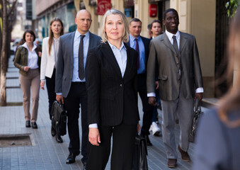 Elegant mature business woman walking on modern city street at rush hour..