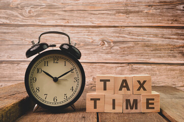 Alarm clock and wooden cubes with word TAX TIME