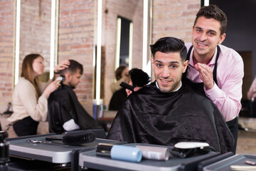 Obraz premium Portrait of skilled hairstylist and satisfied male customer after haircut in modern hair studio