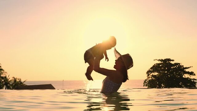 Asian mother and little son enjoying swimming in a swimming pool in summer vacation.