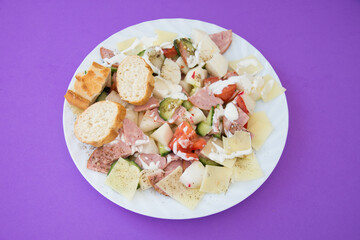 salad with radishes, cheese, tomato pepper cream, cucumber and salami on purple